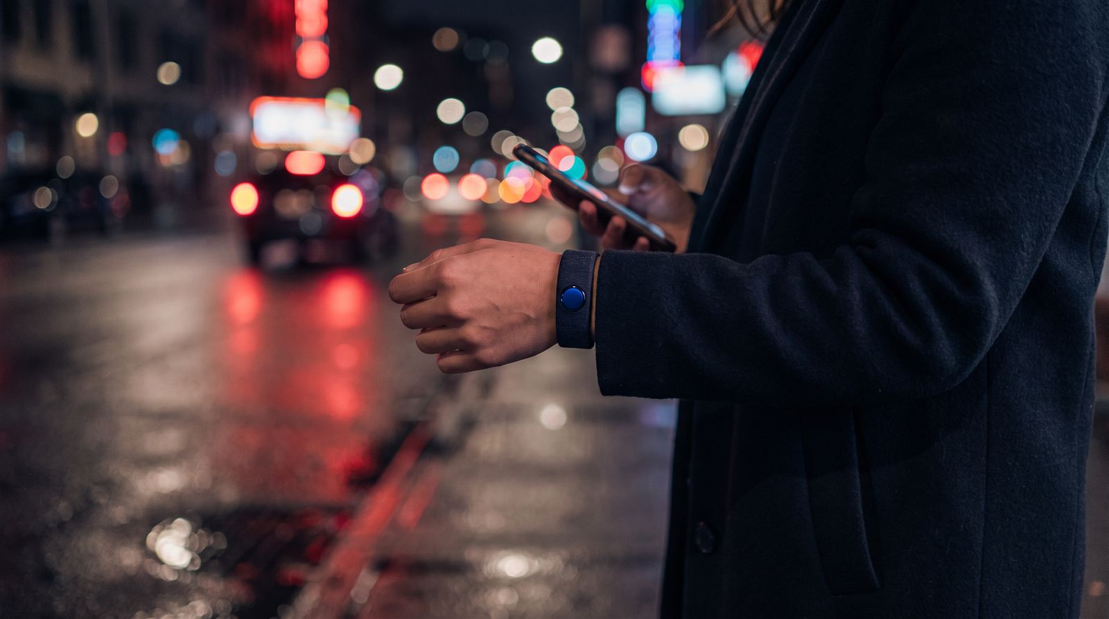 Femme qui appuie discrètement sur le bouton à son poignet, la nuit en ville